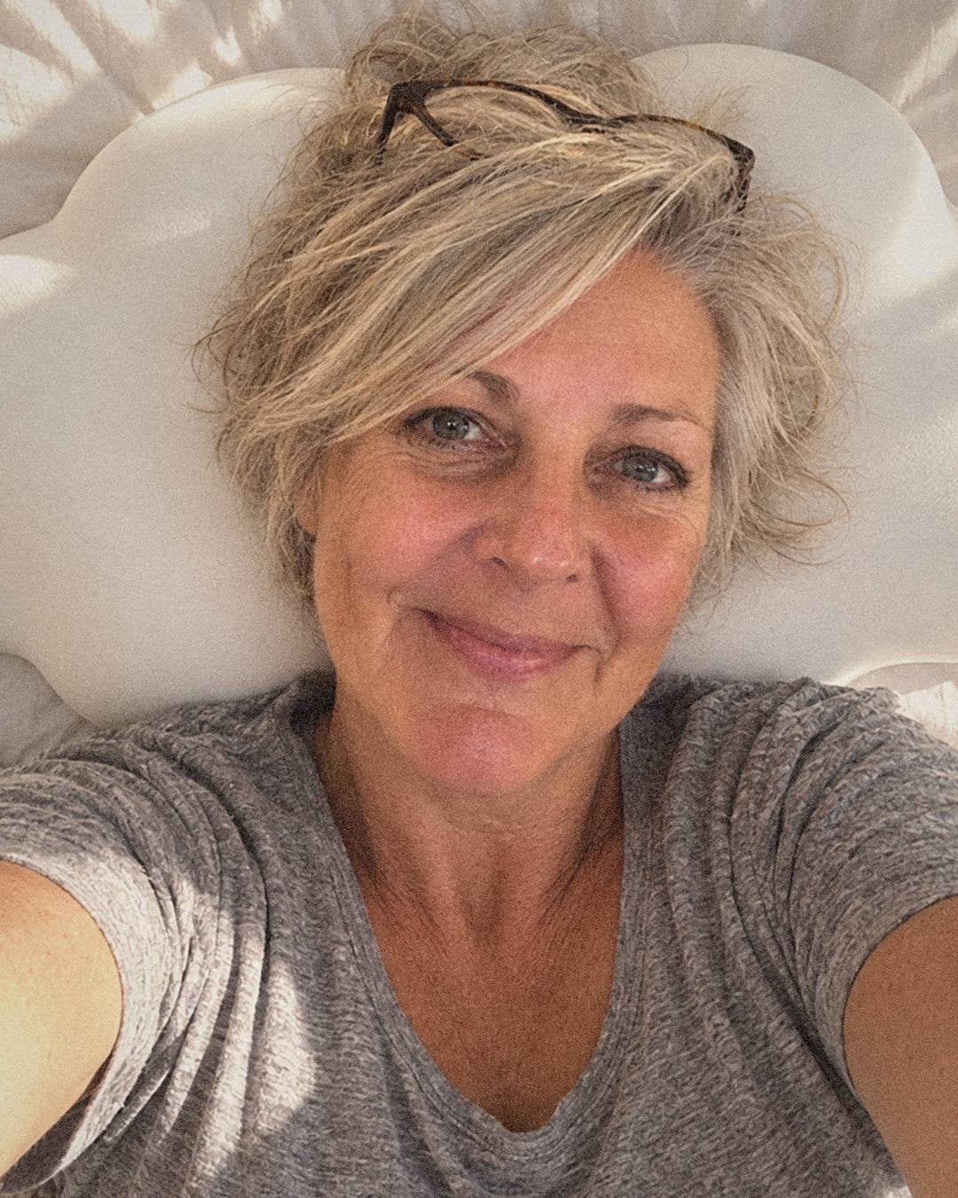 Dana's morning selfie, lying back on her white cloud-shaped Cloud Pillow and smiling