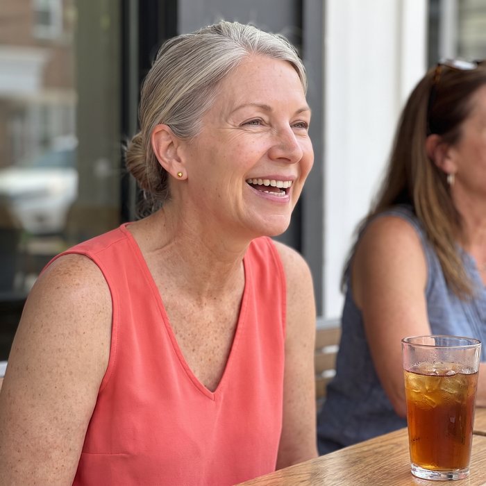 The same woman laughing at lunch in a sleeveless V-neck top, her hair up